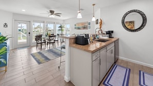 Una cocina moderna con una isla central, luces colgantes y vistas a un balcón.