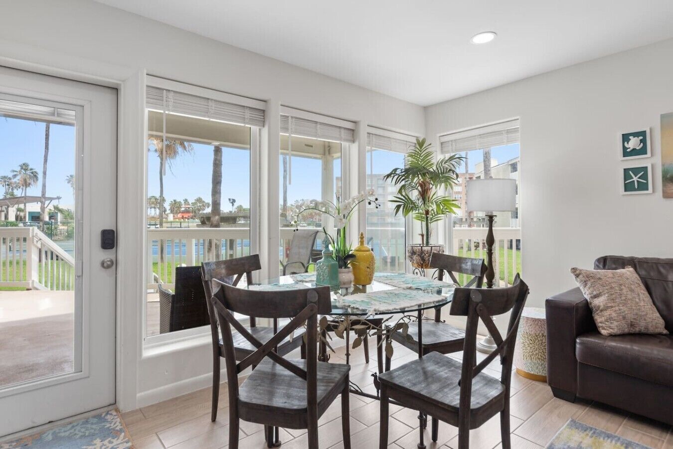 A spacious room with a balcony, a dining table with chairs, a sofa, and a lamp.