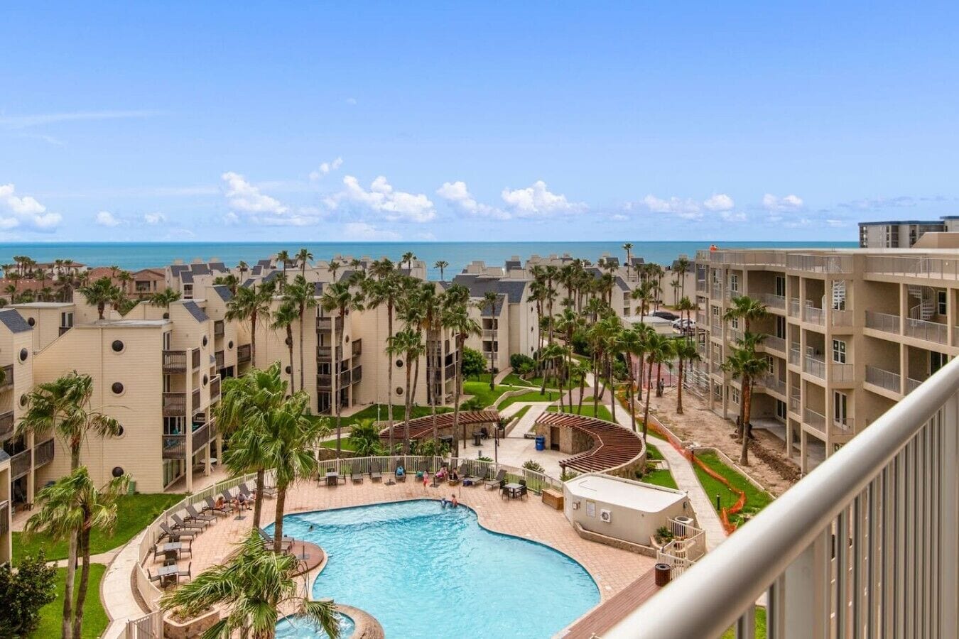 A resort with a pool, palm trees, and a view of the ocean.