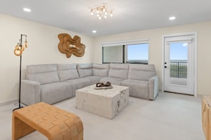 A modern living room with a sectional sofa, a coffee table, a floor lamp, and a large abstract wall art piece. - Designer Beachfront Condo with Endless Ocean Views (South Padre Island)