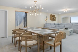 A dining area with a large table, wicker chairs, and a modern chandelier. - Designer Beachfront Condo with Endless Ocean Views (South Padre Island)