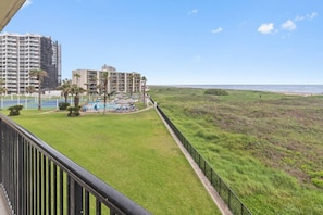 A view of a beachfront property with a pool area, palm trees, and a grassy area. - Designer Beachfront Condo with Endless Ocean Views (South Padre Island)