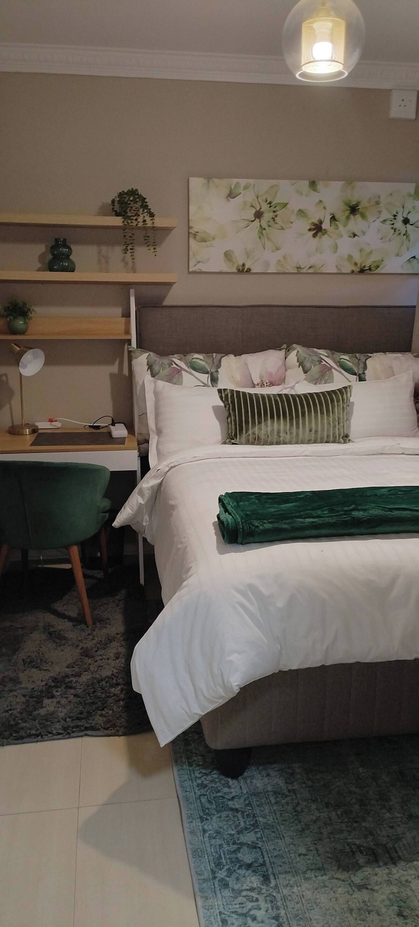 A neatly arranged bedroom with a bed, bedside table, lamp, and a wall-mounted shelf with decorative items.