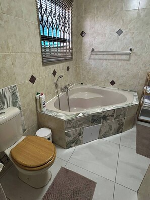 A bathroom with a bathtub, toilet, and window with bars.