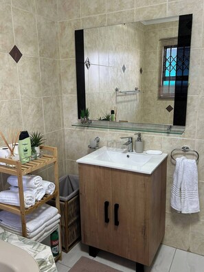 A bathroom with a wooden vanity, a glass shelf, a towel rack, and a mirror.