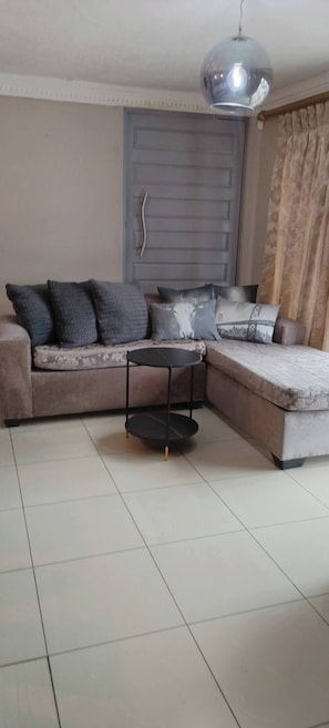 A living room with a sofa, a coffee table, a door, and a curtain.
