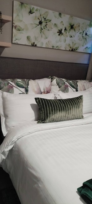 A neatly made bed with white linens and a striped pillow, a floral artwork above it, and a headboard.