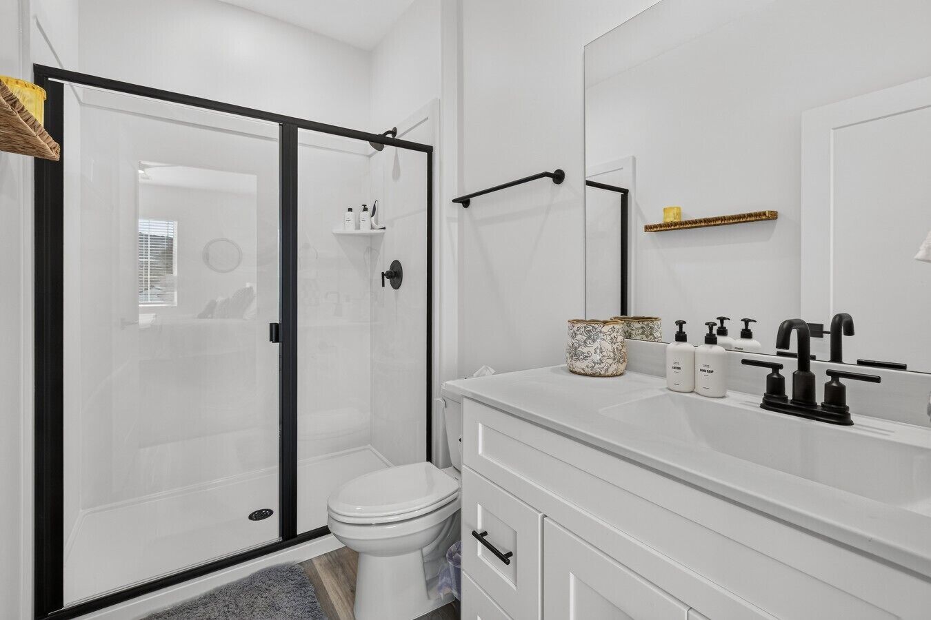 A modern bathroom with a glass-enclosed shower, a white toilet, and a vanity with a mirror and toiletries.