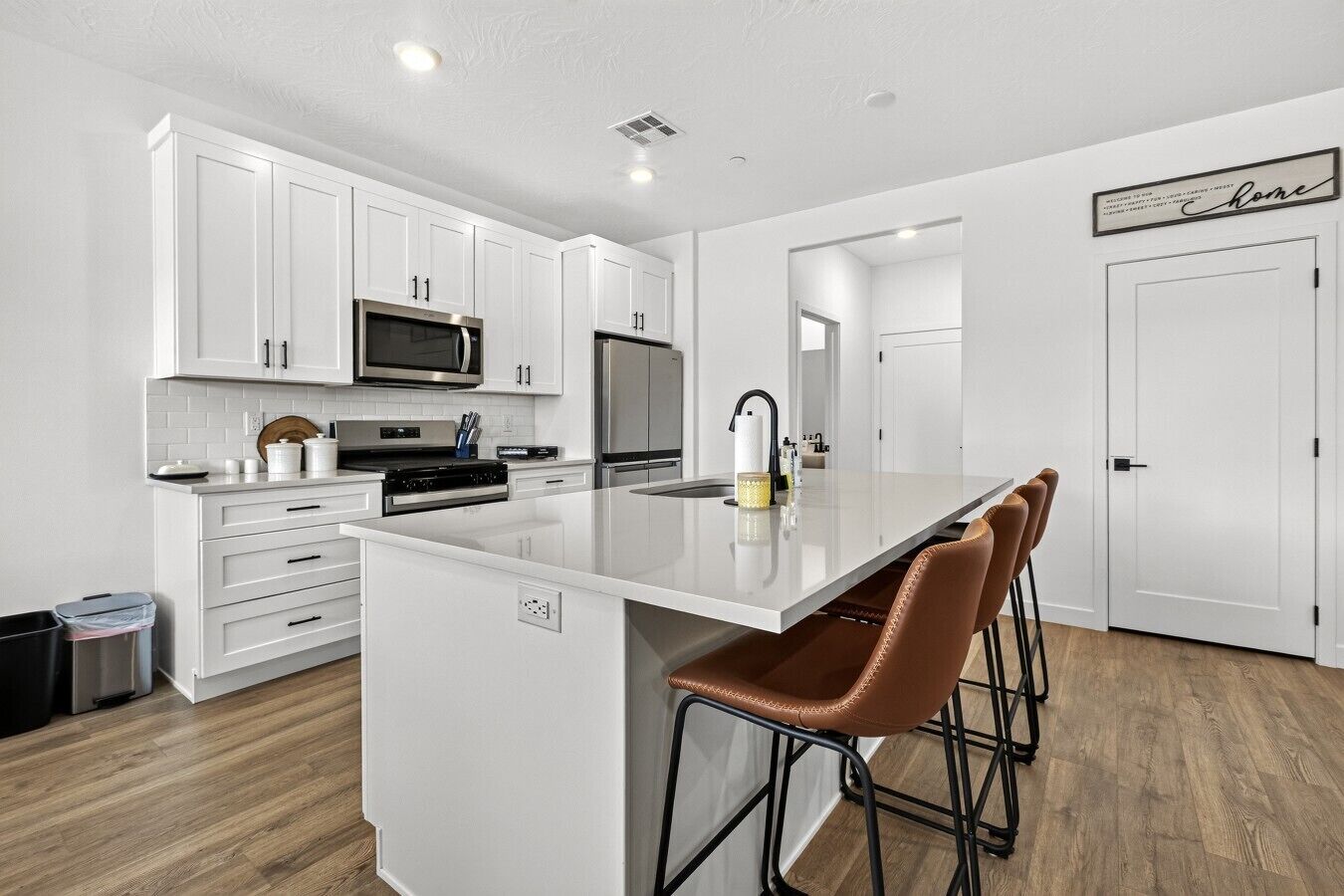 A modern kitchen with white cabinetry, stainless steel appliances, and a central island with bar stools.