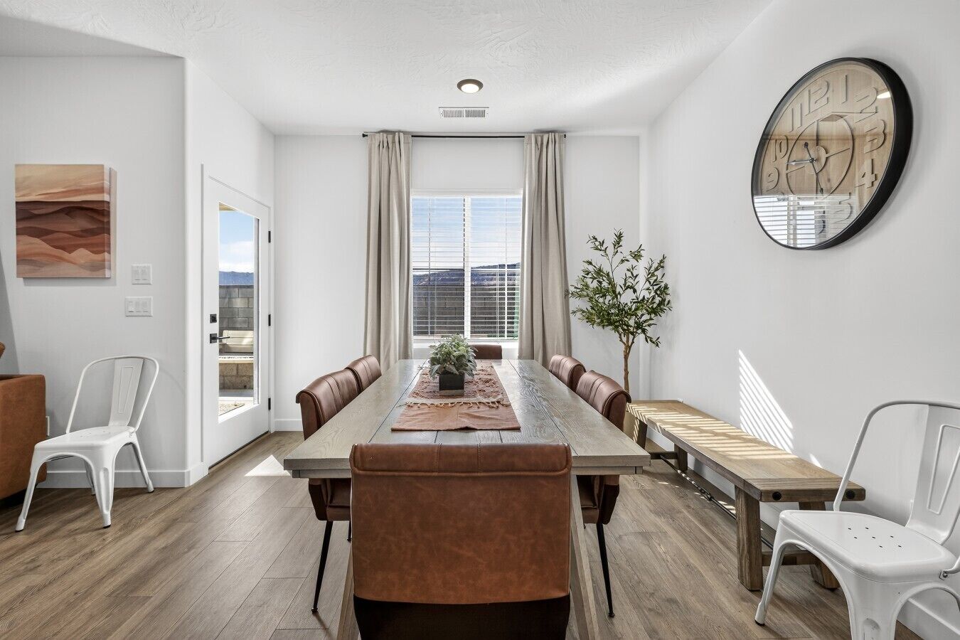 A modern dining room with a long table, chairs, and a potted plant.
