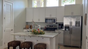 A modern kitchen with white cabinets, a stainless steel refrigerator, a microwave, and a coffee maker. There are three stools at the island. - NICEVILLE FLORIDA
Hammock Haven – Spacious, Serene & Just Minutes from the Beach (Niceville)