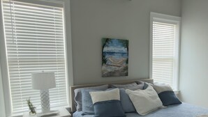 Una camera da letto con un letto, un comodino, una lampada, un condizionatore d'aria e un quadro appeso al muro.