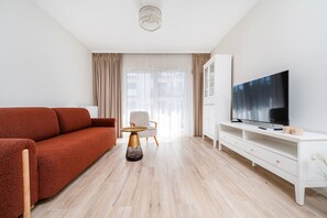 Ein modernes Wohnzimmer mit einer Couch, einem Fernseher, einem weißen Schrank und einem Sessel.