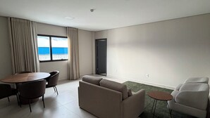 Un salon moderne avec un canapé, une table à manger et des chaises. Il y a une grande fenêtre avec des rideaux, un téléviseur à écran plat fixé au mur et une petite table ronde.