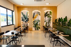 Un comedor moderno con mesas y sillas, una zona de estar verde y vistas a palmeras a través de un panel de madera.