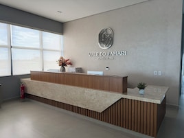 Um balcão de recepção moderno com acabamento em madeira e bancada de mármore, um logotipo fixado na parede e uma janela que oferece iluminação natural.