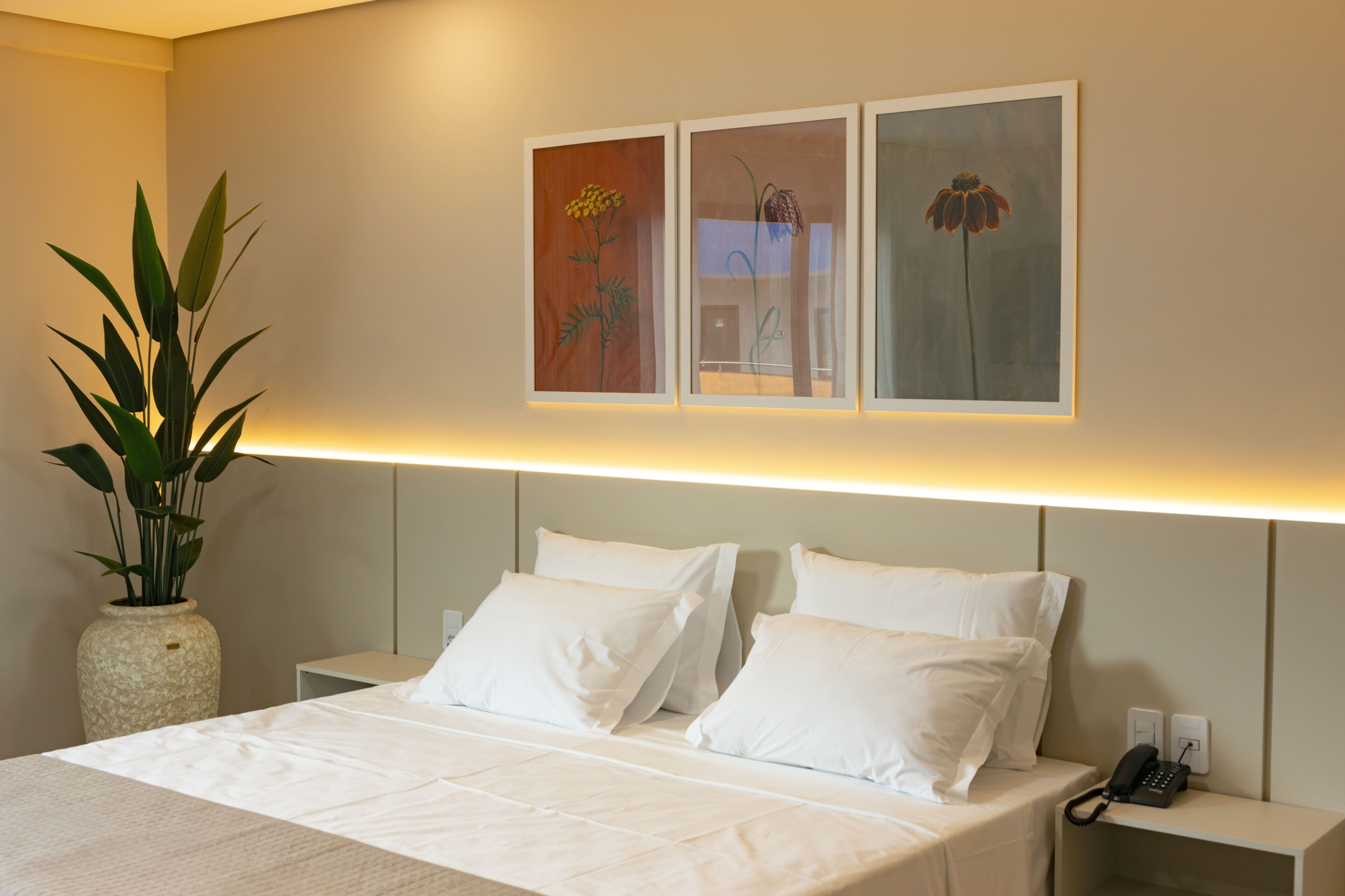A hotel room with a bed, white pillows, a nightstand with a phone, and a wall-mounted artwork.