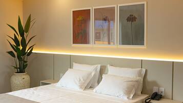 A hotel room with a bed, white pillows, a nightstand with a phone, and a wall-mounted artwork.
