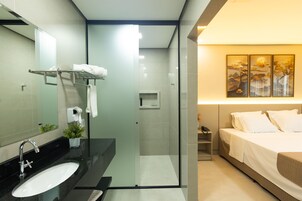 Un baño moderno con cabina de ducha de vidrio, un lavabo con espejo y una mesita de noche con lámpara.