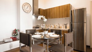 A modern kitchen with a stainless steel refrigerator, wooden cabinets, a round dining table with chairs, and a wall clock. - New! 2BR w/ City Views in Makati & Fast Wi-Fi! (Makati)