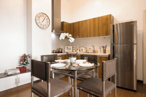 Eine moderne Küche mit einem Edelstahlkühlschrank, Holzschränken, einem runden Esstisch mit Stühlen und einer Wanduhr.