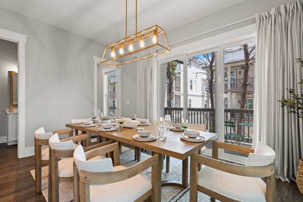 Un coin repas avec une table en bois dressée pour six personnes, des chaises blanches et un luminaire suspendu moderne.