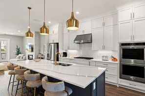 A modern kitchen with white cabinets, stainless steel appliances, and a central island with bar stools. - New Build 30A Home | 5BR Sleeps 12 | Rooftop Hot Tub & Cold Plunge (Inlet Beach)