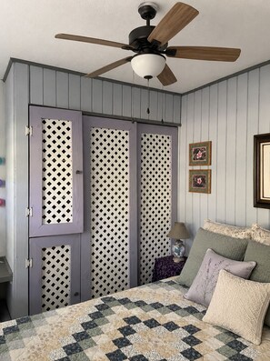 Ein Schlafzimmer mit Bett, Deckenventilator, Nachttisch und Kommode mit Klappentür.