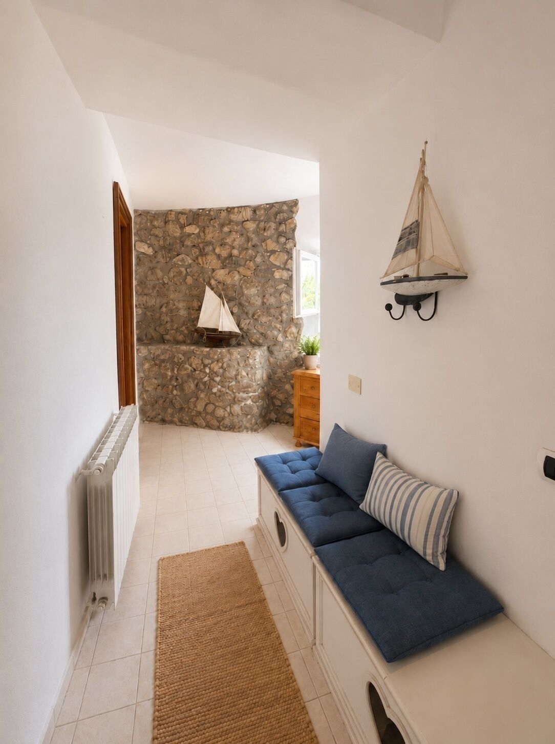 A room with a stone wall, a blue sofa, a small table with a plant, and a wall-mounted sailboat decoration.