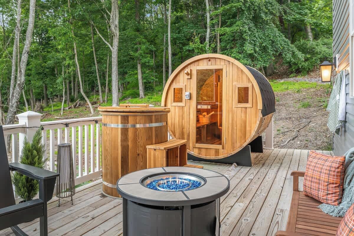 A wooden sauna with a door, a round hot tub, and a deck with outdoor furniture.