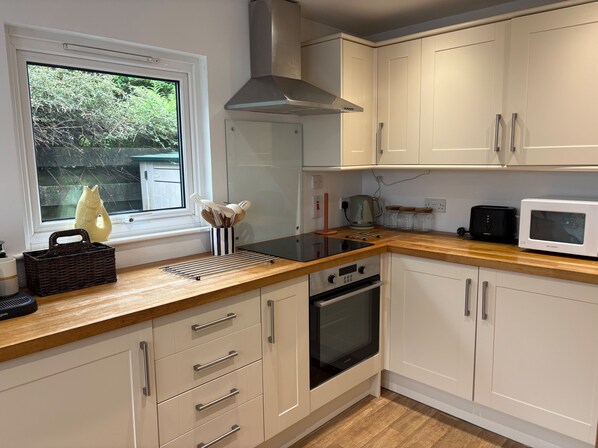 A modern kitchen with white cabinets, a built-in oven, a microwave, and a window with a view of greenery.
