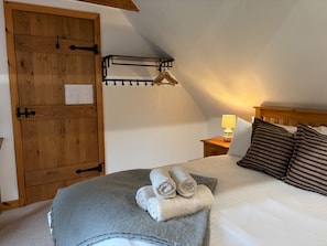 Un dormitorio con puerta de madera, cama con manta gris y toallas enrolladas, mesita de noche con lámpara y lámpara colgante.