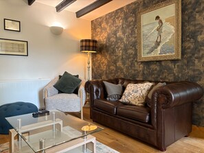A living room with a brown leather sofa, a glass coffee table, a grey armchair, and a lamp.