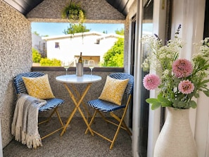 Ein Balkon mit zwei Stühlen, einem Tisch und einem Blumenstrauß.
