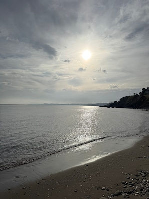 Une plage avec une mer calme, un ciel dégagé et un soleil radieux.