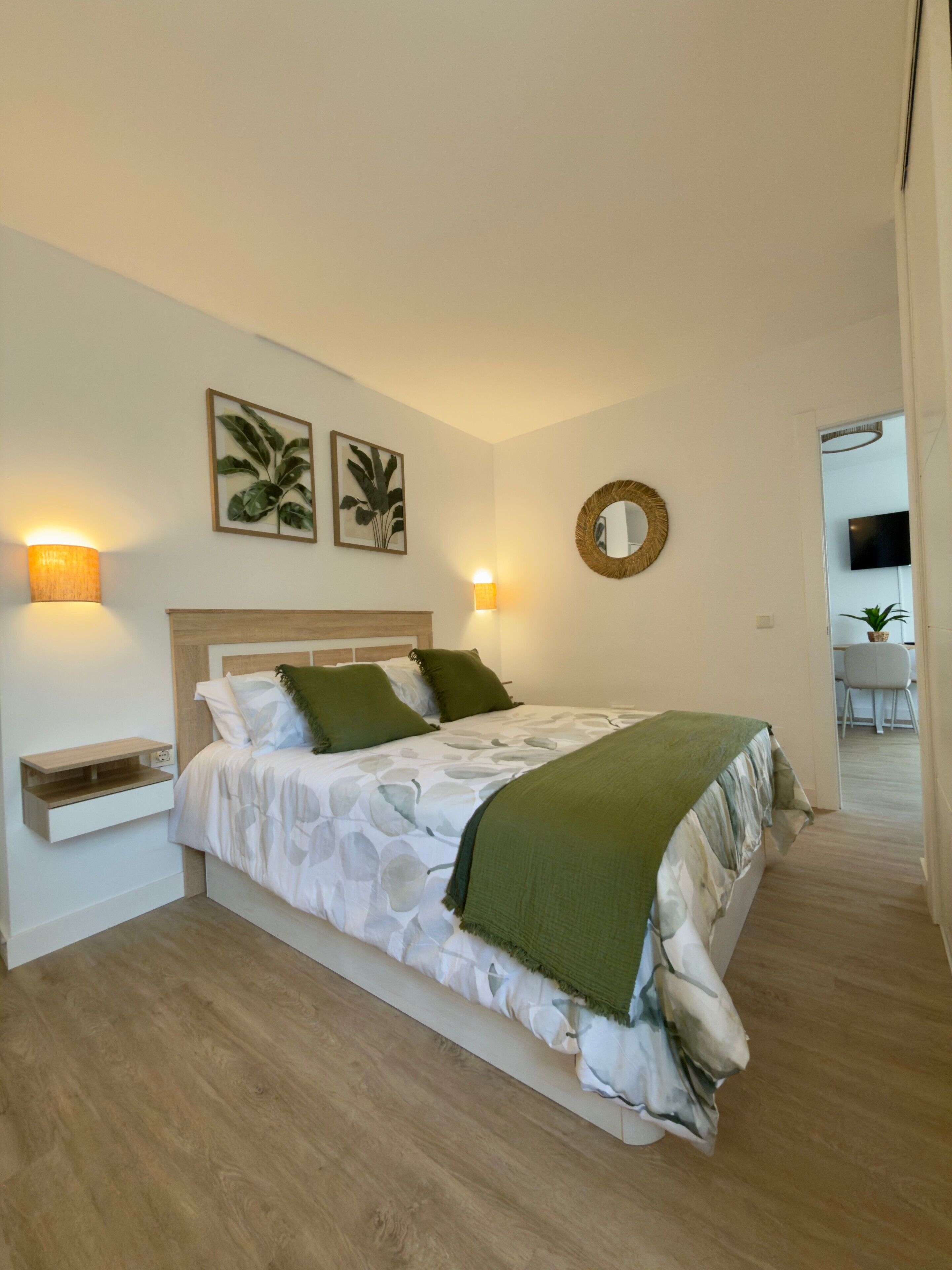 Ein Schlafzimmer mit Bett, Nachttischen, Wandlampen, einem Spiegel und einer Pflanze.