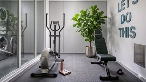 Un gimnasio en casa con equipo de ejercicio, una planta en maceta y decoración de pared motivacional.