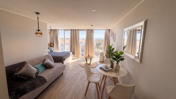 Una sala de estar moderna con un sofá, una mesa de comedor, sillas, una mesita auxiliar y una planta en maceta.