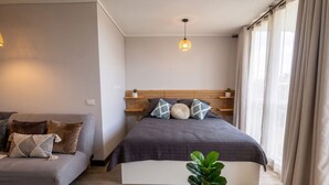 Un dormitorio con cama, sofá, planta en maceta y lámpara colgante.