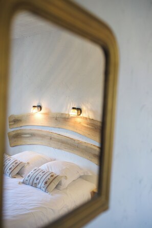 A bed with white bedding and decorative pillows, a wooden headboard, and two wall-mounted lights.