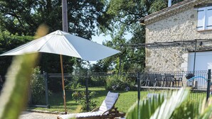 Uma piscina com espreguiçadeira e guarda-sol, rodeada por um edifício de pedra e vegetação.