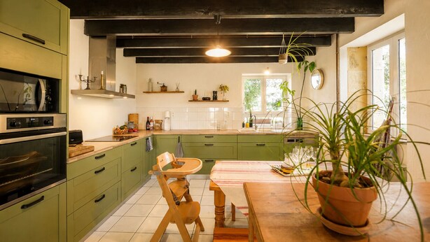Uma cozinha com armários verdes, uma mesa de jantar de madeira e uma planta em vaso.