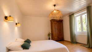 Quarto com cama, guarda-roupa de madeira, luminária pendente e janela com cortinas.