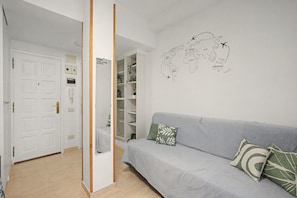 Ein Zimmer mit grauem Sofa, einer Weltkarte an der Wand und einer weißen Tür mit kleinem Fenster.