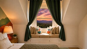 A bedroom with a bed, a window seat with cushions, a lamp, and a view of a sunset. - Luxury Retreat| Theater, Golf, Spa, Firepit & Views (Ahwahnee)