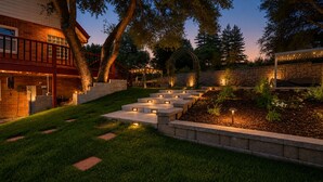 A well-lit outdoor area with steps leading to a covered seating area, surrounded by a stone wall and greenery. - Luxury Retreat| Theater, Golf, Spa, Firepit & Views (Ahwahnee)