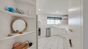 Une cuisine moderne avec des meubles blancs, un réfrigérateur en acier inoxydable et une fenêtre équipée de stores.