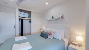Une chambre d’hôtel avec un lit, un téléviseur posé sur un meuble, une armoire et une table de chevet avec une lampe.
