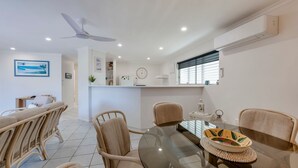 Une pièce moderne et bien éclairée, avec une table à manger, des chaises, un ventilateur de plafond et une fenêtre équipée de stores.