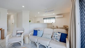 A modern living room with a sofa, chairs, a small table, and a ceiling fan. - 1/20 Bauer Street Bargara (Bargara)